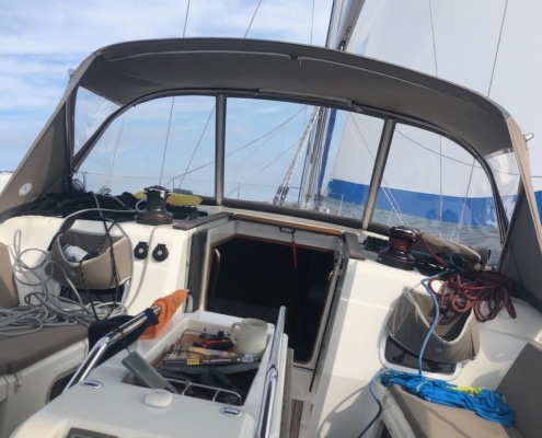 Sailboat cockpit view with ropes, instruments, and open hatch under clear blue skies on a sunny day at sea.