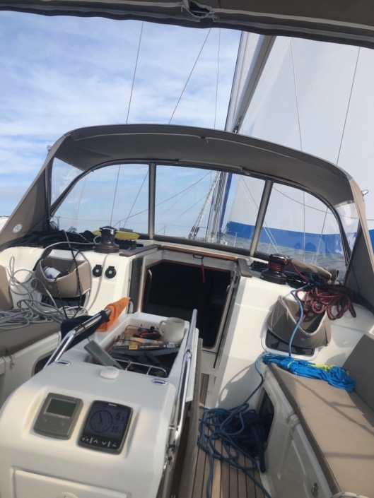 Sailboat cockpit view with ropes, instruments, and open hatch under clear blue skies on a sunny day at sea.