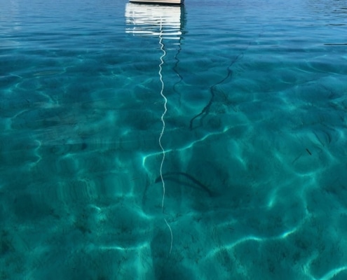 Sailboat anchored on calm turquoise waters, reflecting clear skies, perfect for serene sailing adventures.