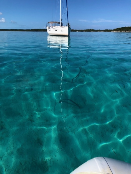 Sailboat anchored on calm turquoise waters, reflecting clear skies, perfect for serene sailing adventures.