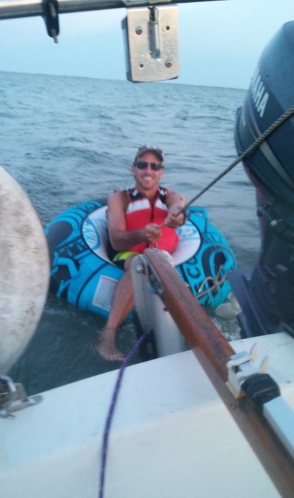 Man in a life jacket tubing behind a boat on the ocean, holding a rope with a smile.