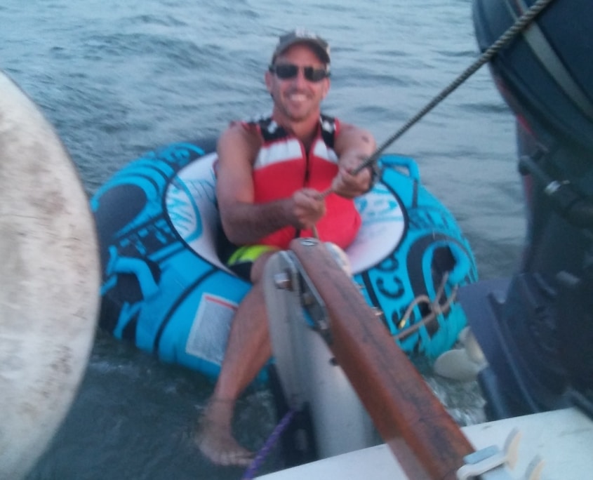 Man in a life jacket tubing behind a boat on the ocean, holding a rope with a smile.