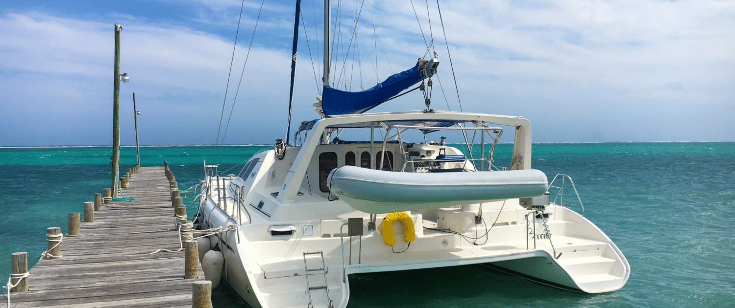 Catamaran anchored at a wooden pier on turquoise seas under a clear blue sky, ideal for a serene sailing getaway.