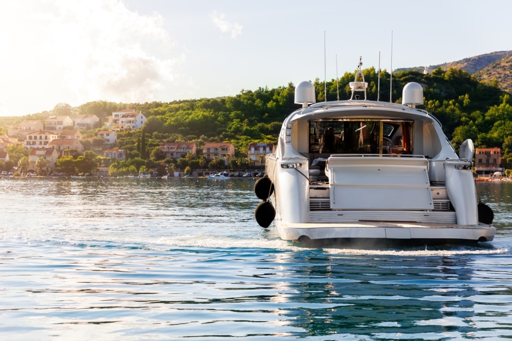 Luxury yacht cruising near scenic coastal village under a clear sky, showcasing an idyllic Mediterranean lifestyle.