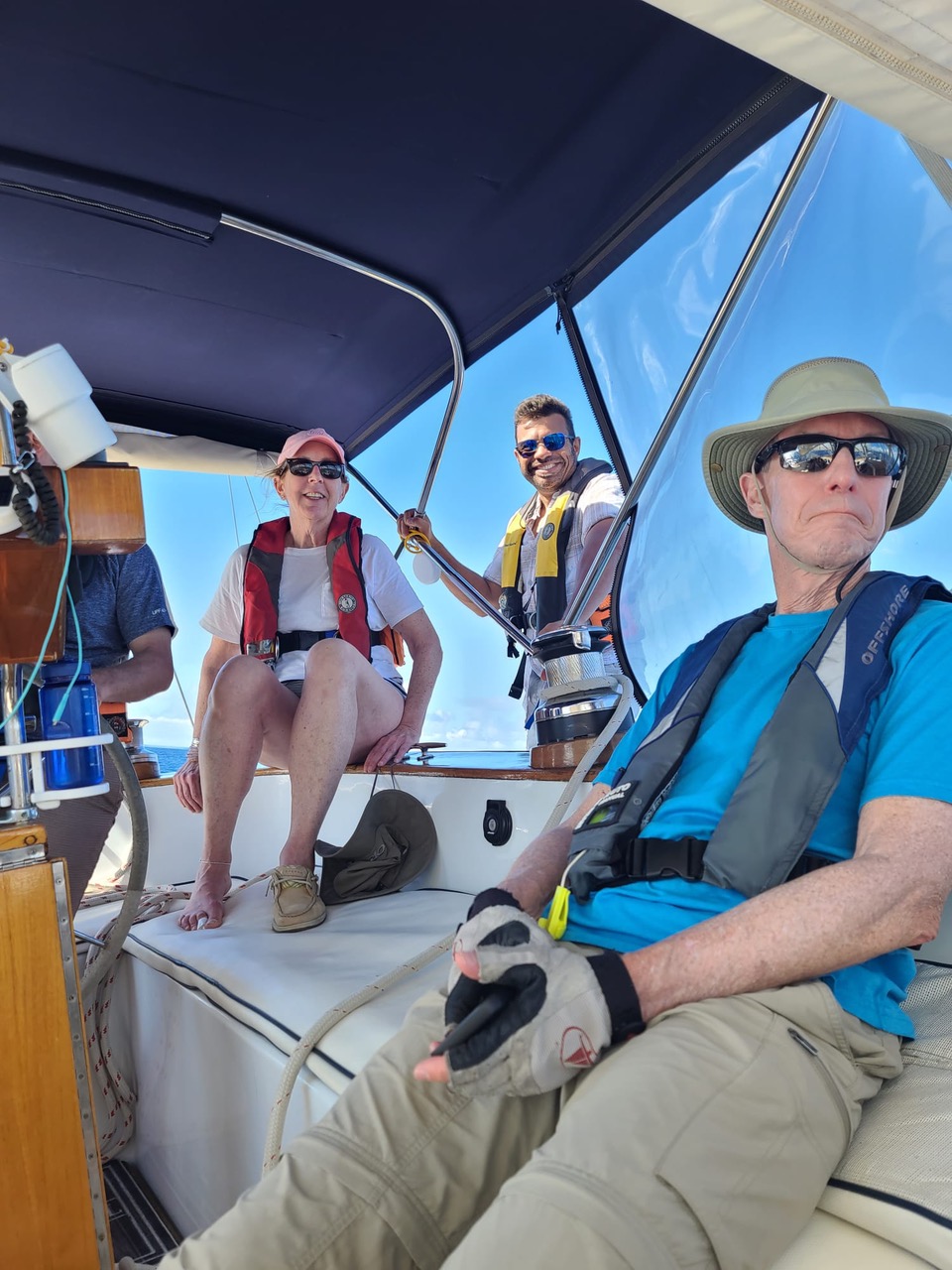Group enjoying a sunny day sailing, wearing lifejackets and hats under a boat's canopy.