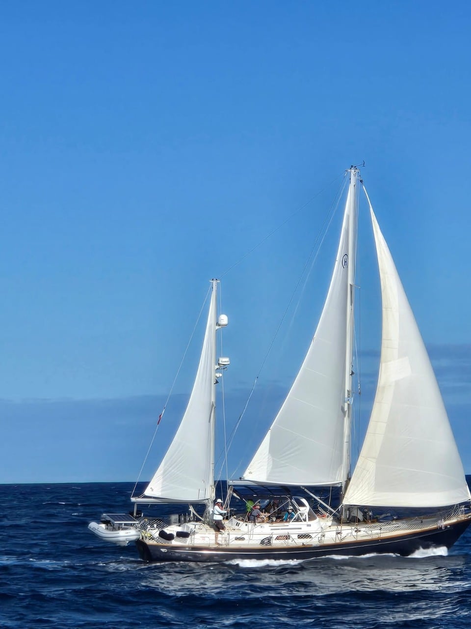 Sailboat cruising across the ocean with white sails against a clear blue sky, ideal for adventurous sailing enthusiasts.