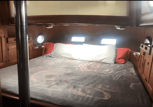 Cozy sailboat cabin with a plush bed, wood paneling, and porthole windows. Perfect for a restful sea voyage.