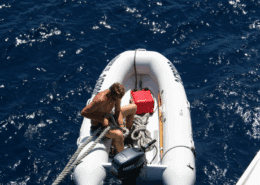 Man securing rope on inflatable boat in open sea; sunny day with deep blue water. dinghy gas vs electric motor