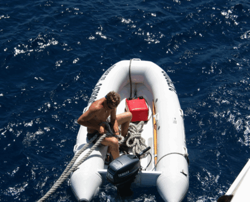Man securing rope on inflatable boat in open sea; sunny day with deep blue water. dinghy gas vs electric motor