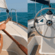 Split image: Left shows a hand on a wooden tiller, right displays a yacht's steering wheel on clear ocean waters. Tiller vs. Wheel: The Real-World Take