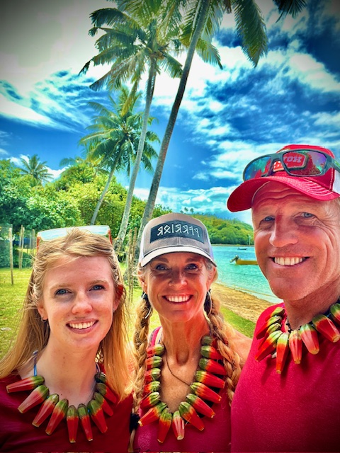 A joyful group enjoying a tropical beach with palm trees and ocean in the background, all wearing matching vibrant necklaces.