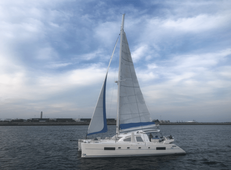 Sleek white catamaran sailing on calm waters under a clear, blue sky near the coast.