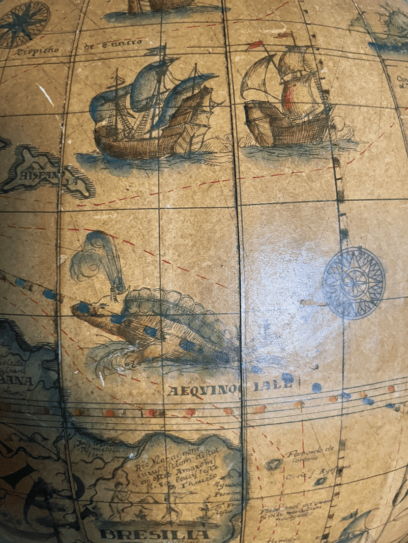 Antique maritime globe detail featuring historic ships and sea routes near the equator, with artistic oceanic creatures.