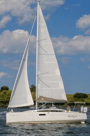 White sailboat cruising on open water under a clear blue sky with puffy clouds and distant green hills.