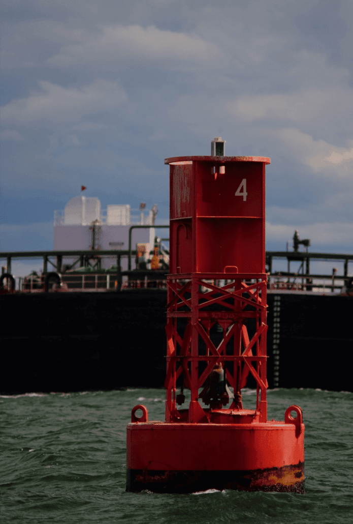Red buoy in ocean near large ship, marking safe navigation channel under cloudy sky.