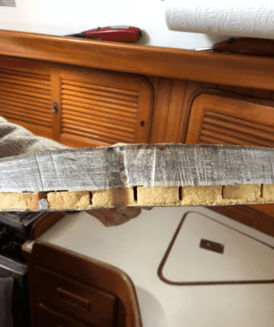 Damaged sailboat interior wood panel with visible core material, showing delamination and wear.