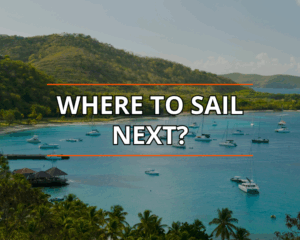 Tropical bay with anchored sailboats under clear sky, lush hills backdrop; text reads Where to Sail Next?