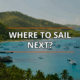 Tropical bay with anchored sailboats under clear sky, lush hills backdrop; text reads Where to Sail Next?