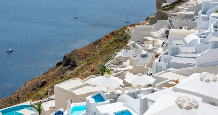 Seaside view of white Cycladic buildings and sailboats in Santorini, Greece, under a clear blue sky.
