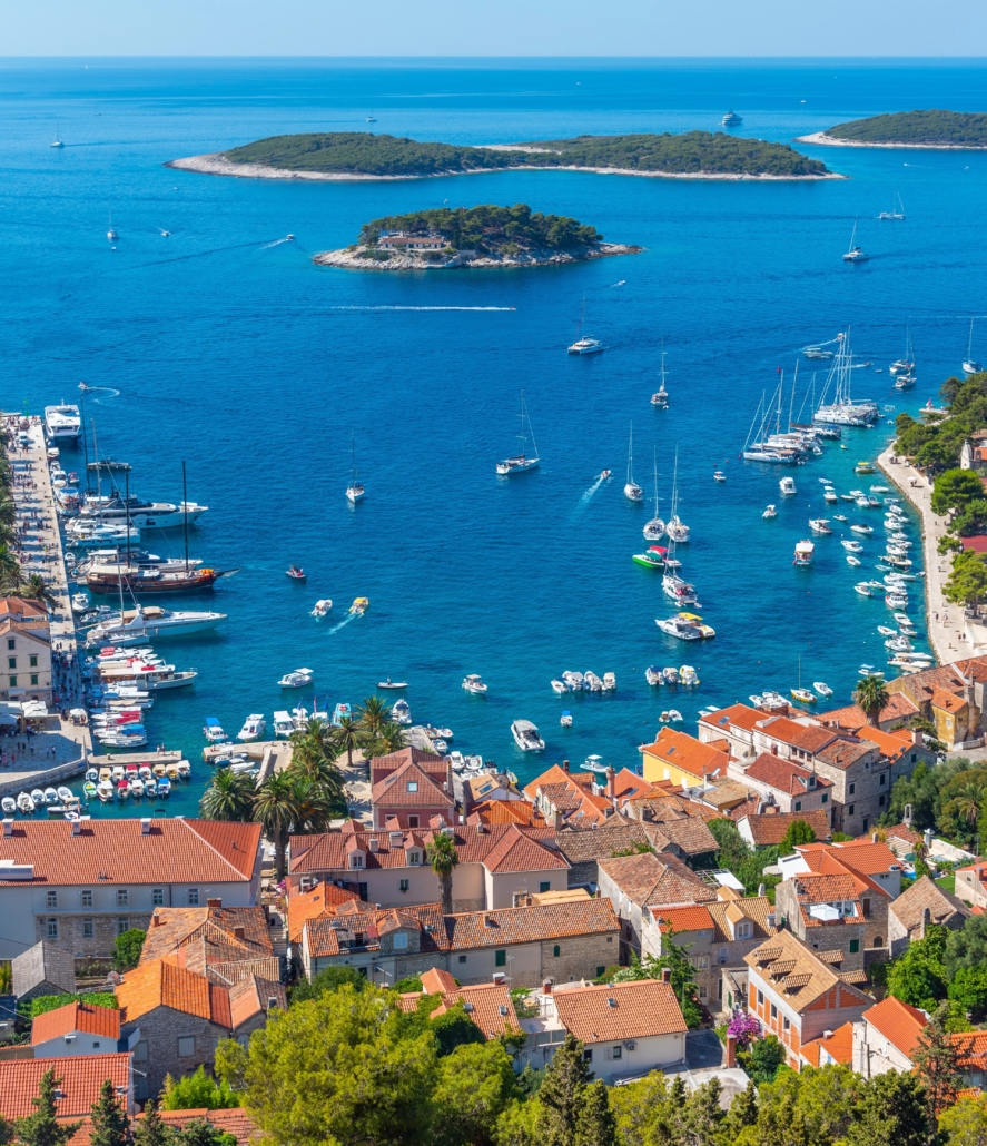 Coastal town with yachts and sailboats docked in the azure waters, near lush islands under a sunny blue sky.