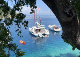 Sailboats anchored in clear blue water, surrounded by lush greenery in a tropical paradise.