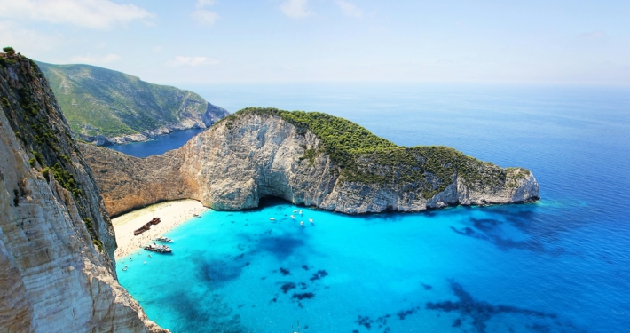 Scenic view of Navagio Beach with turquoise water, cliffs, boats, and a shipwreck in Zakynthos, Greece.