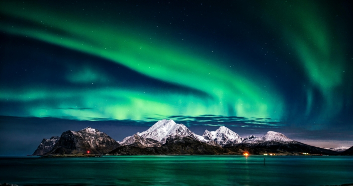 Aurora borealis lights up the Arctic sky over snowy mountains and calm sea. Ideal sailing view.