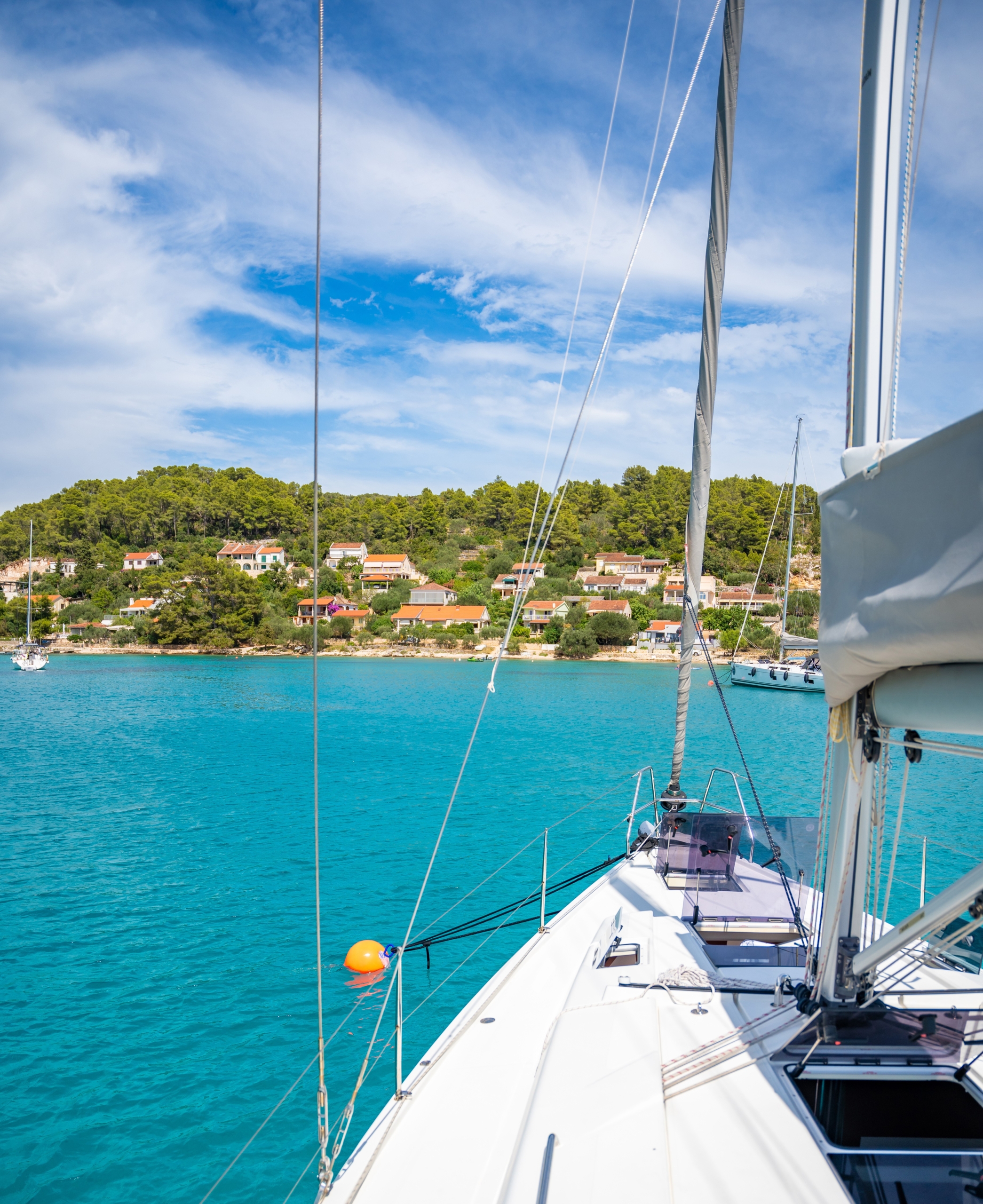 Sailboat navigating turquoise waters toward a coastal village. Scenic sailing adventure, clear skies, and picturesque landscapes.
