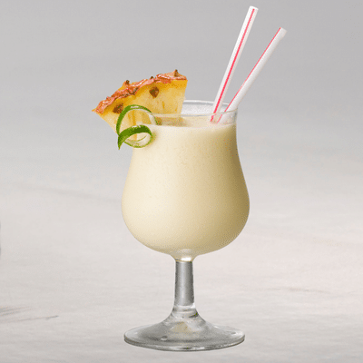 Creamy tropical cocktail in a glass with pineapple garnish and lime twist, perfect for a refreshing sailboat escape.