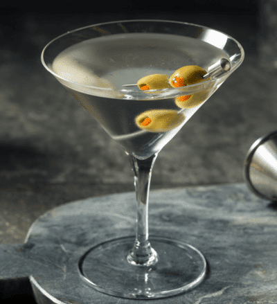 Classic martini with olives on a skewer in a sleek glass, set on a textured surface, perfect for a cocktail party.