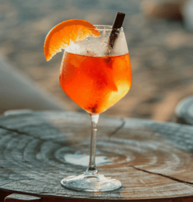 Refreshing Aperol Spritz with orange slice on a beachside table, capturing the essence of coastal relaxation.