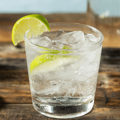 Refreshing cocktail with lime slice and ice in a glass on rustic wood table, perfect for a summer sailing day.