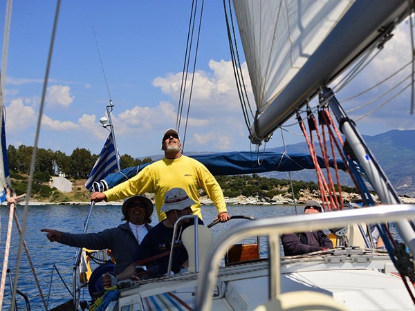 Group sailing a yacht on a sunny day, enjoying the coastal view. Adventure on the sea, sails unfurled, teamwork in action.