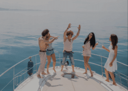 Group of friends dancing on yacht deck, enjoying a sunny day at sea with drinks, laughter, and carefree fun on a luxury crewed charter