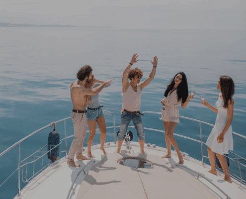 Group of friends dancing on yacht deck, enjoying a sunny day at sea with drinks, laughter, and carefree fun on a luxury crewed charter