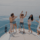 Group of friends dancing on yacht deck, enjoying a sunny day at sea with drinks, laughter, and carefree fun on a luxury crewed charter
