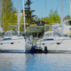 Two sailboats docked side by side in a tranquil marina, surrounded by lush trees and clear skies.