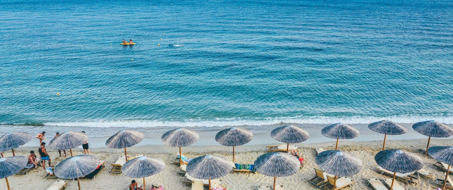 Sandy beach with umbrellas and loungers by the blue sea, islands visible in the distance. Perfect for a relaxing getaway.