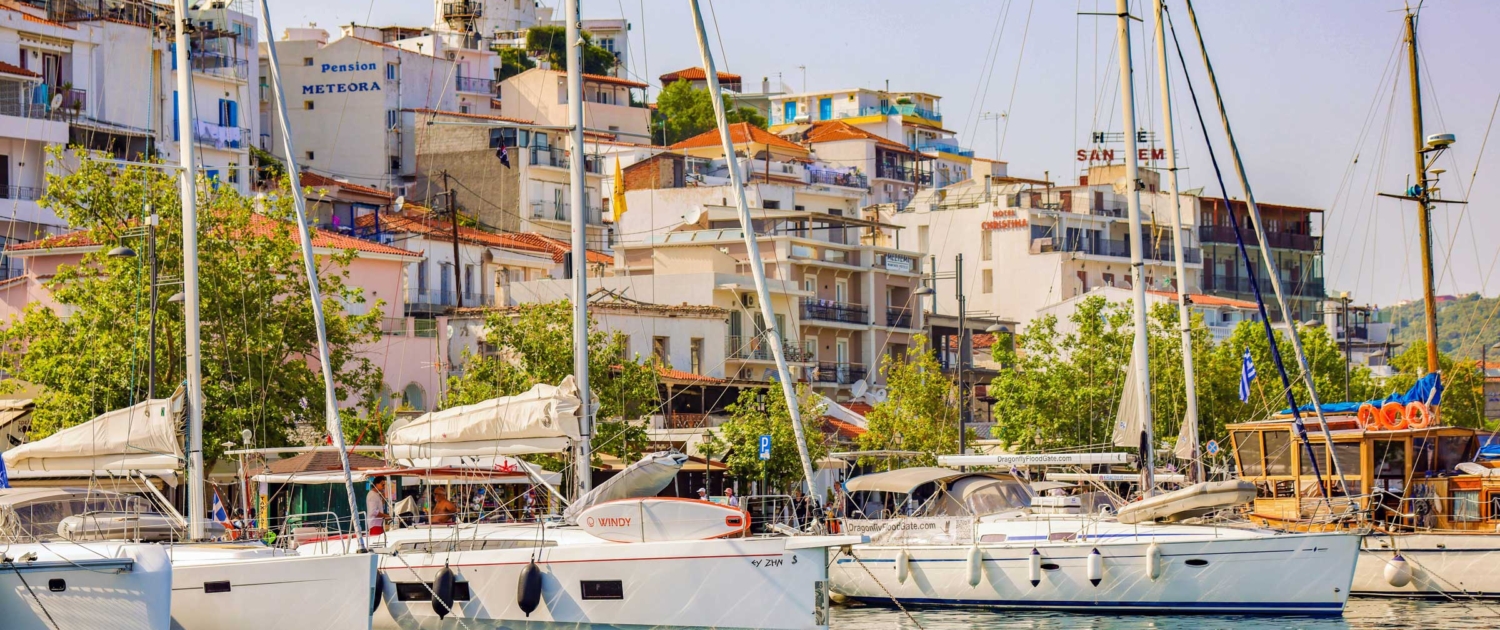 Marina filled with sailboats against a backdrop of colorful coastal buildings under a clear blue sky.