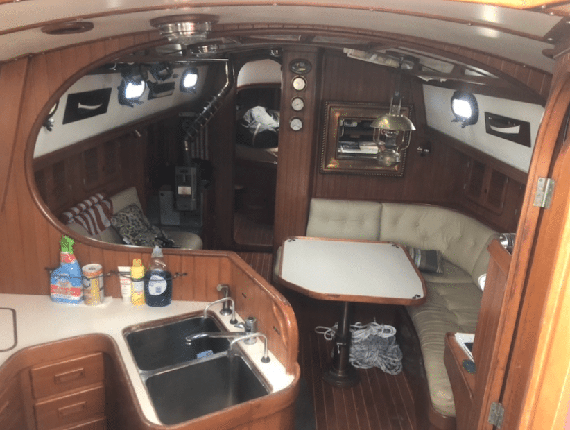Cozy sailboat interior with a galley, sink, and dining area, featuring rich wood paneling and nautical decor.