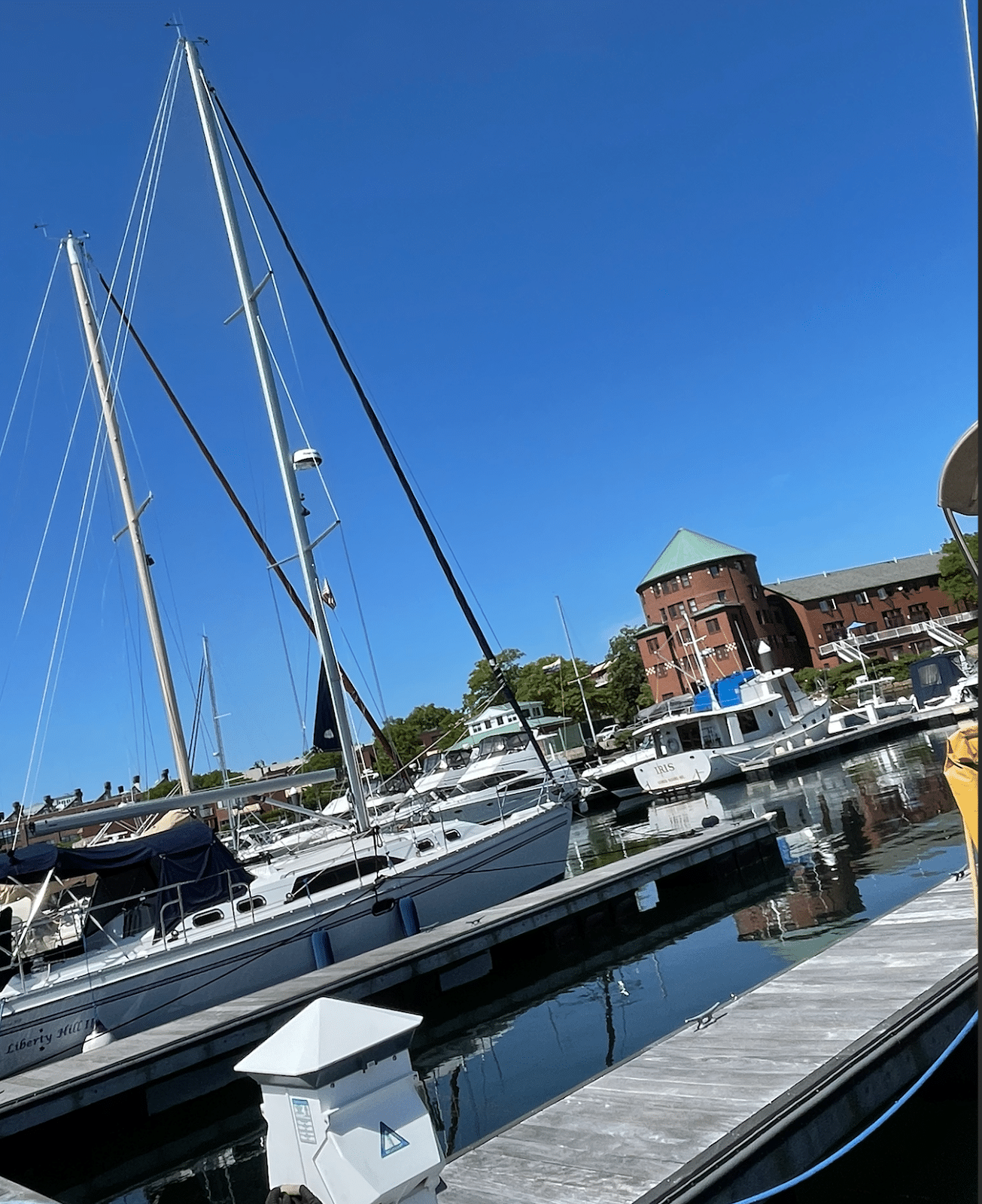 Sailboats docked at a marina under clear blue skies, with a historic brick building in the background.