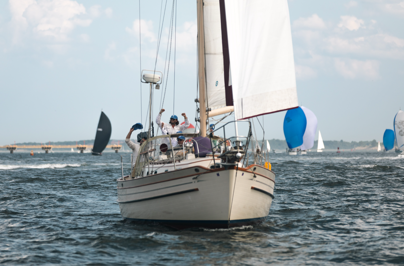 Sailboat race with crew celebrating victory on the water, blue skies, and distant sailboats in the background.