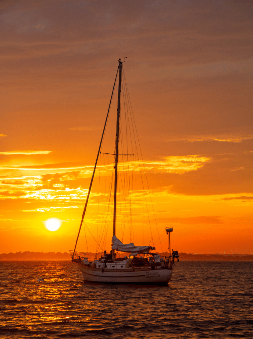 Sailboat at sunset on calm sea, vibrant orange sky, peaceful sailing adventure.