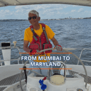 Person sailing with a smile under sunny skies, wearing a red vest and yellow shirt, captioned From Mumbai to Maryland.