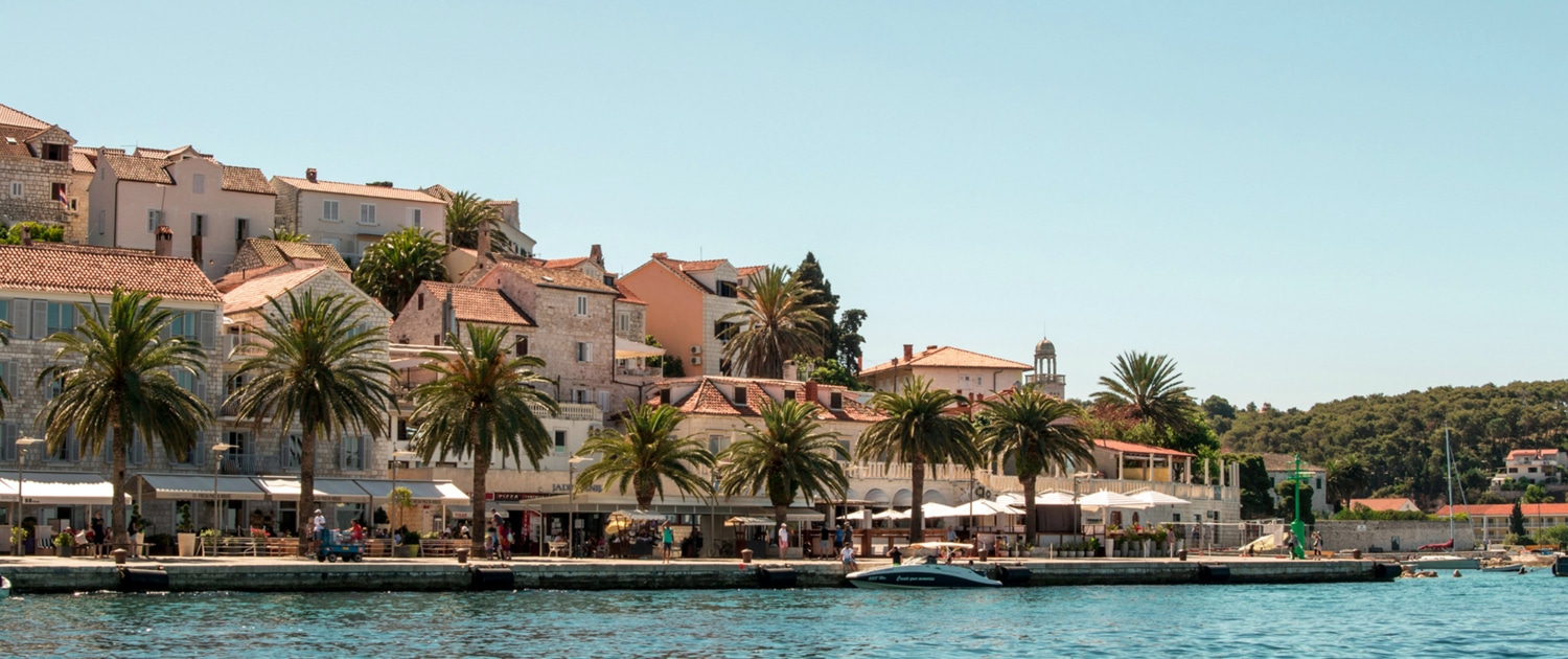 Scenic coastal town with palm trees, charming stone buildings, and waterfront view. Ideal sailing destination.