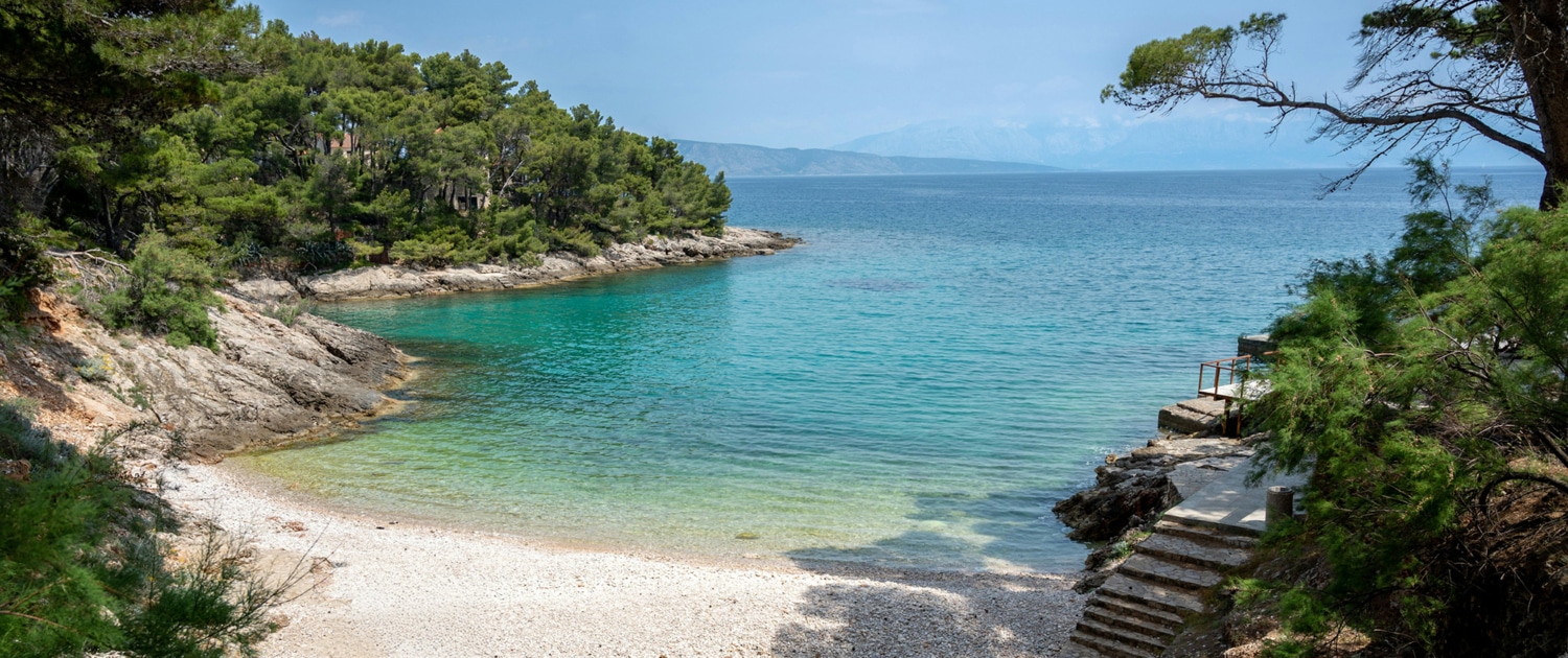 Hidden cove with turquoise water, rocky shoreline, and lush green trees, perfect for serene sailing adventures.