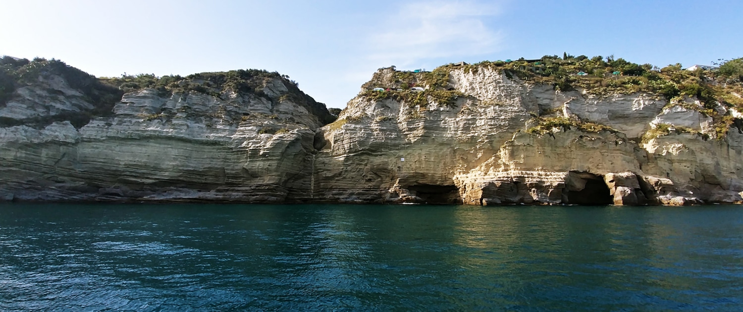 Rocky coastal cliffs and caves along a vibrant blue sea under clear skies, ideal for sailing and exploration.