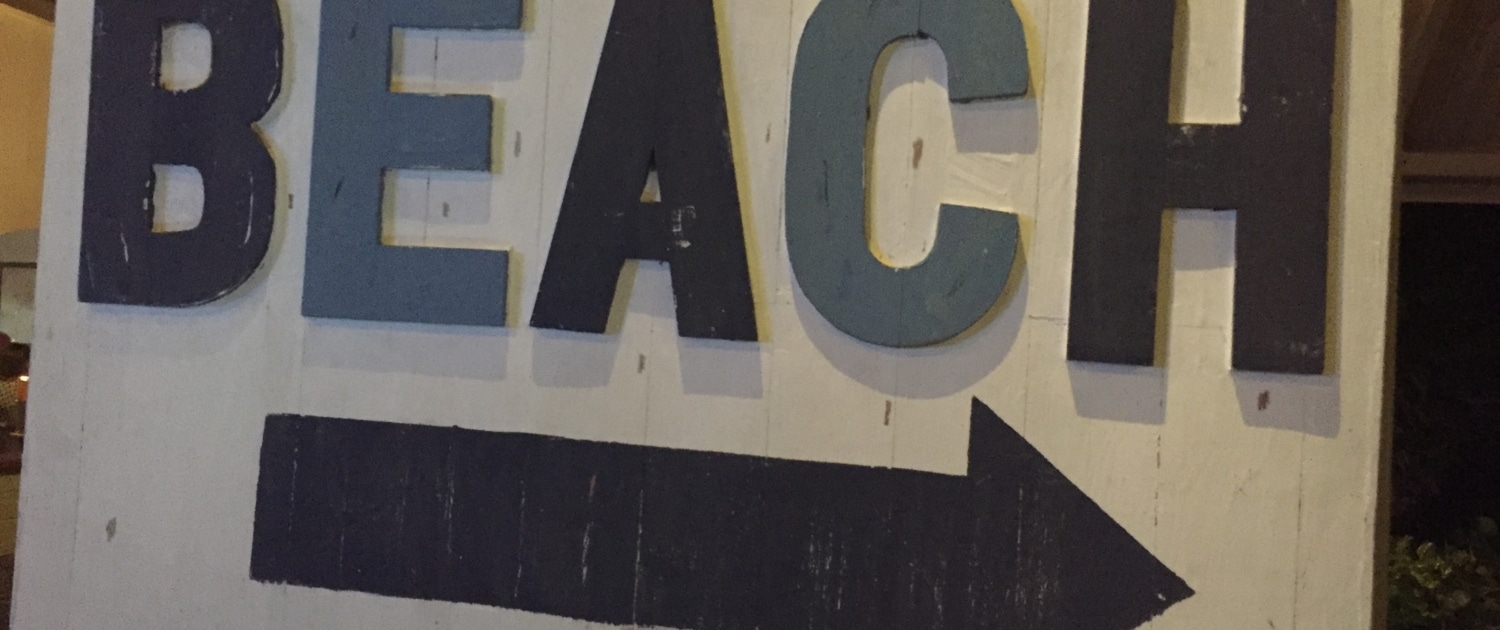 Sign pointing to the beach destination, guiding beachgoers with bold letters and an arrow at night.