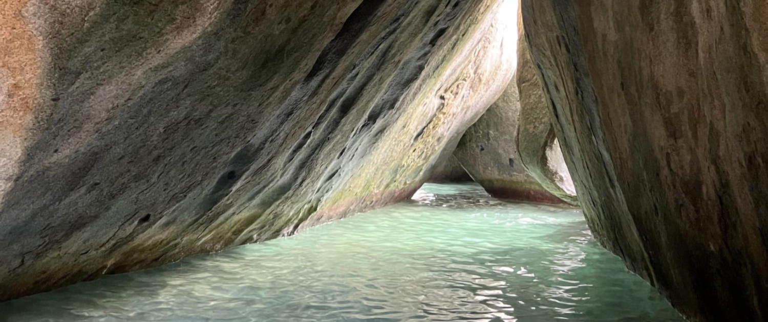 Crystal-clear water under granite boulders in a scenic coastal cave, perfect for sailing exploration adventures.
