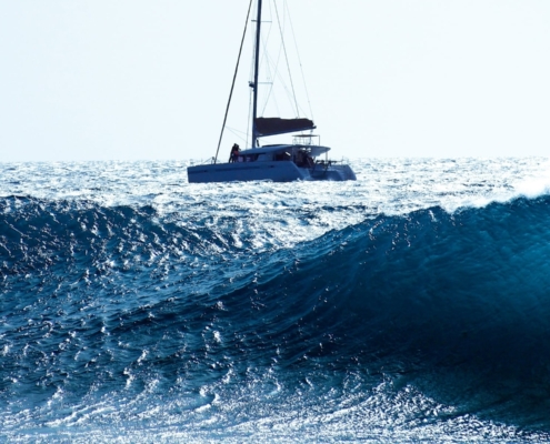Catamaran sailing on vibrant blue ocean waves under clear sky.